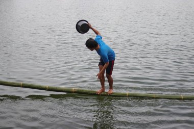 Sukabumi, Batı Java, Endonezya - 22 Ağustos 2021: Endonezyalı bir adam bambu üzerinde yürümeye çalışırken suya düşer ve Endonezya Bağımsızlık Günü boyunca Panjat Pinang adı verilen geleneksel oyunları oynamaya çalışır