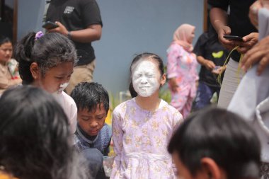 Sukabumi, Batı Java, Endonezya - 19 Ağustos 2021: Endonezyalı tatlı bir kızın yüzü, Endonezya 'nın bağımsızlık gününde Nyiru adlı bir yiyecek konteynerinden para almak için yarışırken buğday dolu.
