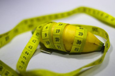A small banana is wrapped with measuring tape isolated on white background. Conceptual illustration for men penis size. Sex Education, health and medical concept