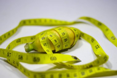 A small banana is wrapped with measuring tape isolated on white background. Conceptual illustration for men penis size. Sex Education, health and medical concept