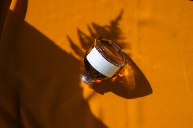 Beyaz etiketli 50 ml 'lik parfüm şişesi ve dokulu turuncu kumaş arka planında yeşil yapraklar. Parfüm şişesi fotoğrafı.