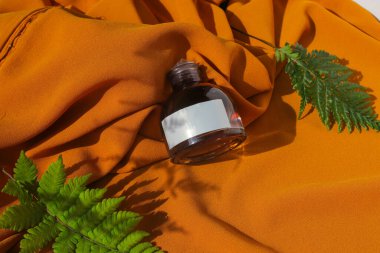 Beyaz etiketli 50 ml 'lik parfüm şişesi ve dokulu turuncu kumaş arka planında yeşil yapraklar. Parfüm şişesi fotoğrafı.