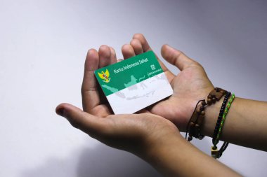 Sukabumi, Batı Java, Endonezya - 14 Ekim 2021: Asyalı bir kızın eli Endonezya 'dan Kartu Sehat' ı (KIS veya Sağlık Sigorta Kartı) beyaz arka planda tutuyor.