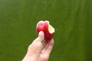 Elin yarısı yenmiş kırmızı elma ve yeşil bulanık arka plan.