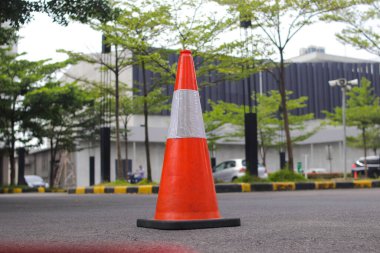 Alışveriş merkezinin otoparkında gri asfalt üzerinde beyaz ve turuncu çizgili trafik konisi.