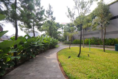 Bandung 'daki alışveriş merkezinin parkında beton tuğlalar ve yeşil ağaçlarla dolu bir yol.