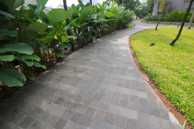 Bandung 'daki alışveriş merkezinin parkında beton tuğlalar ve yeşil ağaçlarla dolu bir yol.