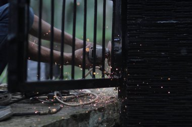 Bir adam elektrikli kaynak makinesi ile metali kaynak yaparak çitleri tamir eder. Kaynakçı, kaynak metali ve metalle uğraşır.