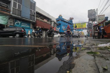 Sukabumi, Batı Java, Endonezya - 22 Eylül 2020: Kırmızı tesettürlü genç bir Asyalı kadın salgın sırasında kalabalık arasında su birikintileriyle sokakta yürüyor.