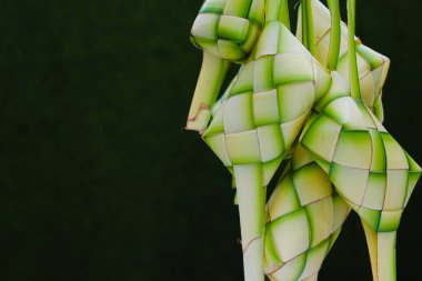 Bir grup boş ketupat derisi ya da ketupat kesesi. Telif alanı ve yeşil arkaplan. Ketupat genellikle Hari Raya ya da bayram zamanında servis edilir. Ketupat kesesi örülmüş genç hindistan cevizi yapraklarından yapılır.
