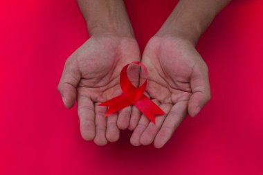 Hand holding a Red AIDS Ribbon with copy space for text isolated on red background. World AIDS Day, symbol of the fight against HIV, AIDS and cancer, Healthcare and medical background concept.