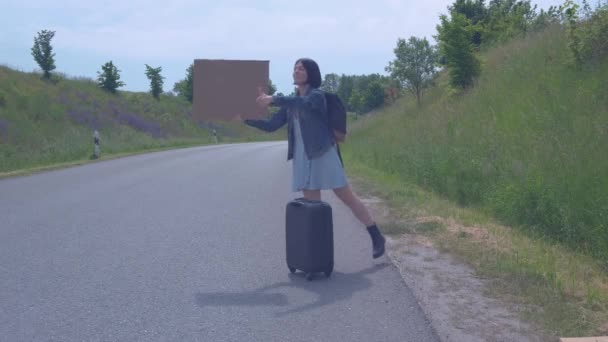 Концепция путешествия и хитчхокинга. Молодая девушка, которая автостопом останавливает машину на дороге. — стоковое видео