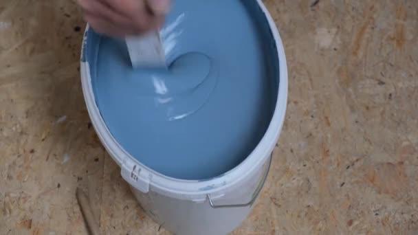Die Hände eines Mannes mit einem Stock rühren die Farbe in einem Eimer an Blaue Farbe tropft in den Eimer. — Stockvideo