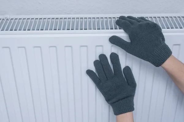 Woman in gloves warming hands on heating radiator
