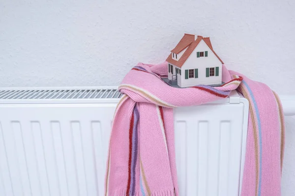 Huismodel verpakt in sjaal op radiator binnen. Verwarmingsseizoen prijs — Stockfoto