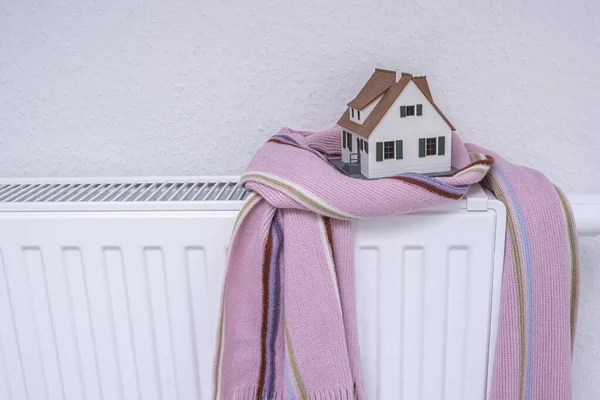 Huismodel verpakt in sjaal op radiator binnen. Verwarmingsseizoen prijs — Stockfoto