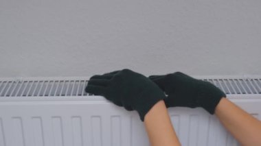 Bir kadın ellerini duvarın yanındaki ısıtıcı kaloriferde ısıtıyor. Apartman soğuk.