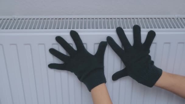 A woman warms his hands on a heating radiator near the wall. Cold in the apartment — Vídeo de Stock