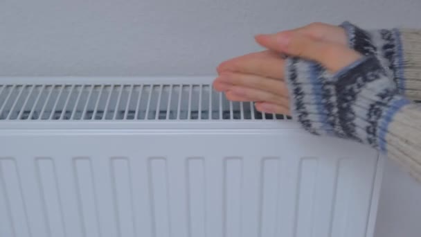 女性は壁の近くの暖房ラジエーターで手を暖める。アパートの寒さ — ストック動画
