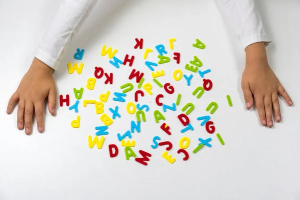 Colorful letters. The childs hands lay out colored letters on the table. Soon to school. School learning concept