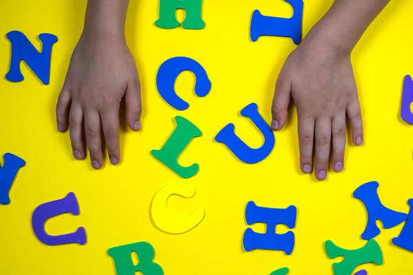 Colorful letters of the alphabet on yellow background. Primary school or preschool, kindergarten. Childs hands near the letters. Back to school soon
