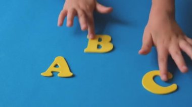 Childs hand playing with letters of the alphabet. School start. Yellow letters on a blue background