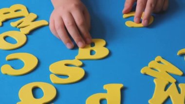 Childs hand playing with letters of the alphabet. School start. Yellow letters on a blue background