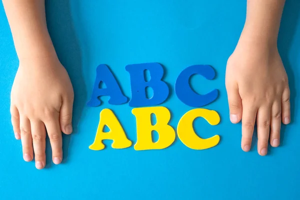 Back to school supplies and letters on a blue background. Beginning of the school year. Blue yellow colors. childs hands. Blue yellow colors