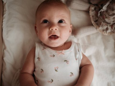 Yeni doğmuş bir bebek soyunma masasında yatar ve gülümser, kameraya bakar.