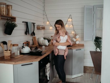 Anne ve bebek. Kollarında çocuğu olan bir anne yemek hazırlıyor, çocuk maması.