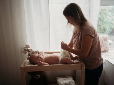 Anne ve bebek. Annem yeni doğan bebekle soyunma masasında oynuyor.