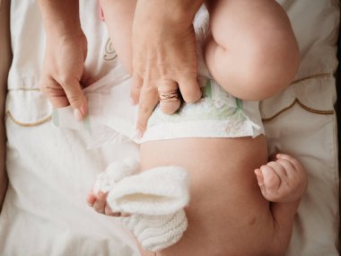 Anne ve bebek, anne masanın üzerinde bebeğin bezini değiştiriyor.