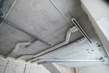 İnşaat halindeki bir evin beton tavanındaki havalandırma borularının kabloları. Odanın inşaatı devam ediyor. Duvarları alçılı, zemini betondan ve tavanı da betondan..