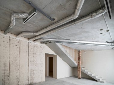 Odanın inşaatı devam ediyor. Duvarları alçılı, zemini beton. İnşaat halindeki bir evin beton tavanına havalandırma boruları döşenmiş..