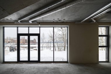 Odanın inşaatı devam ediyor. Duvarları alçılı, zemini beton. Beton bir tavanda havalandırma boruları ve inşaat halindeki bir binada panoramik pencereler..