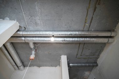İnşaat halindeki bir evin beton tavanındaki havalandırma borularının kabloları. Odanın inşaatı devam ediyor. Duvarları alçılı, zemini betondan ve tavanı da betondan..