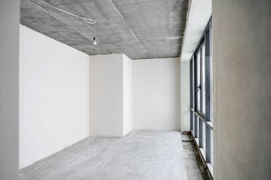 Odanın inşaatı devam ediyor. Duvarları alçılı, zemini beton. Beton bir tavanda havalandırma boruları ve inşaat halindeki bir binada panoramik pencereler..