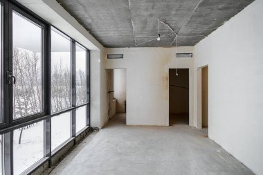 Odanın inşaatı devam ediyor. Duvarları alçılı, zemini beton. Beton bir tavanda havalandırma boruları ve inşaat halindeki bir binada panoramik pencereler..