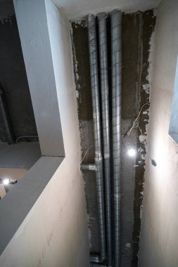İnşaat halindeki bir evin beton tavanındaki havalandırma borularının kabloları. Odanın inşaatı devam ediyor. Duvarları alçılı, zemini betondan ve tavanı da betondan..