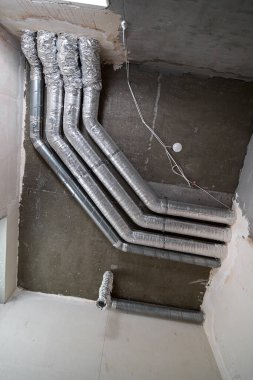 İnşaat halindeki bir evin beton tavanındaki havalandırma borularının kabloları. Odanın inşaatı devam ediyor. Duvarları alçılı, zemini betondan ve tavanı da betondan..