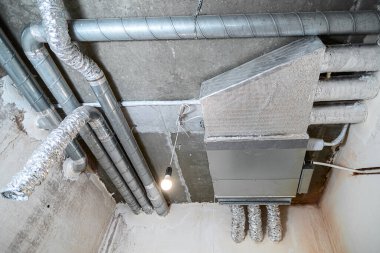 İnşaat halindeki bir evin beton tavanındaki havalandırma borularının kabloları. Odanın inşaatı devam ediyor. Duvarları alçılı, zemini betondan ve tavanı da betondan..