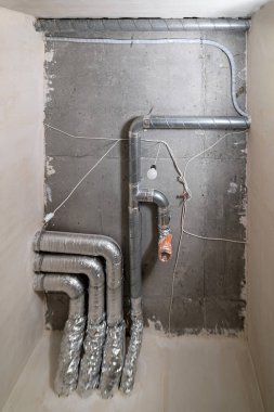 İnşaat halindeki bir evin beton tavanındaki havalandırma borularının kabloları. Odanın inşaatı devam ediyor. Duvarları alçılı, zemini betondan ve tavanı da betondan..