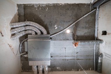İnşaat halindeki bir evin beton tavanındaki havalandırma borularının kabloları. Odanın inşaatı devam ediyor. Duvarları alçılı, zemini betondan ve tavanı da betondan..