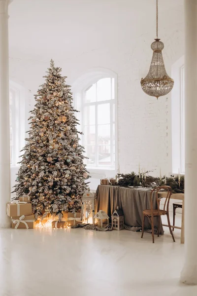 Árvore de Natal coberta de neve com guirlandas coloridas. Os presentes de Ano Novo estão sob a árvore. — Fotografia de Stock