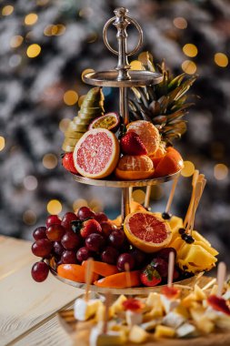 Olgun mandalinalar masanın üzerinde bir tabakta uzanır. Arka planda bulanık bir arka plan vardır. Noel ağacı süsleri ve Noel oyuncakları ile süslenmiştir..