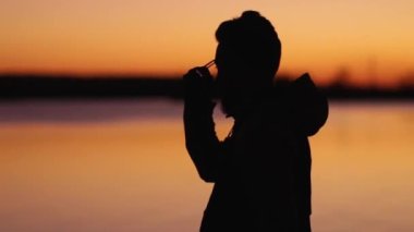 Okyanusun kenarında duran genç bir adam yorgunluktan gözlüklerini çıkarıp tekrar takıyor.