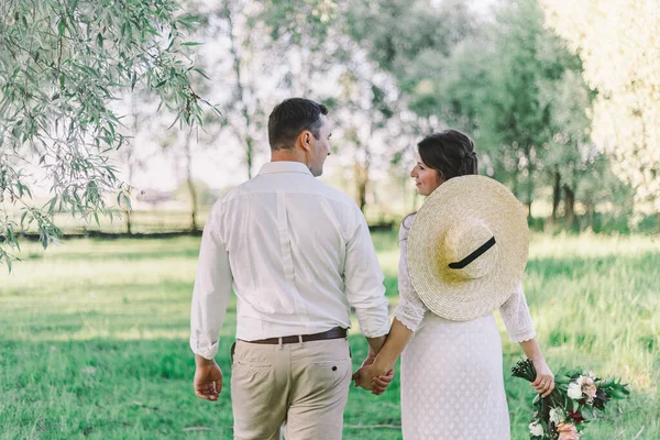 Menyasszony és a vőlegény, séta, és tartja a kezében a réten. Széles látószögű napnyugtakor fénykép. — Stock Fotó