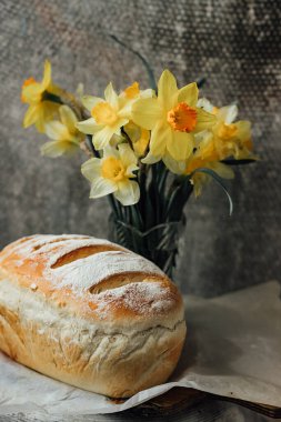 Sadece fırından taze ekmek, parşömen kağıdının üzerinde serinliyor, güzel çiçeklerin yanında.
