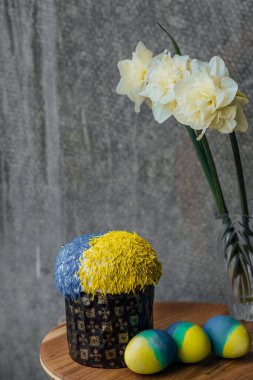 Ukrayna bayrağının renginde lezzetli Paskalya pastası, arka planda çiçekler olan ahşap bir masada sarı-mavi Paskalya yumurtaları. mesaj için yer. seçici odak.