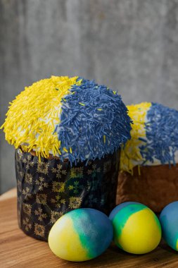 Ukrayna bayrağının renginde lezzetli Paskalya pastası, arka planda çiçekler olan ahşap bir masada sarı-mavi Paskalya yumurtaları. mesaj için yer. seçici odak.